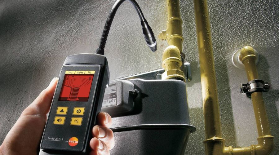 Hand holding gas leak detector near yellow gas pipes, illustrating gas leak detection for homeowners.