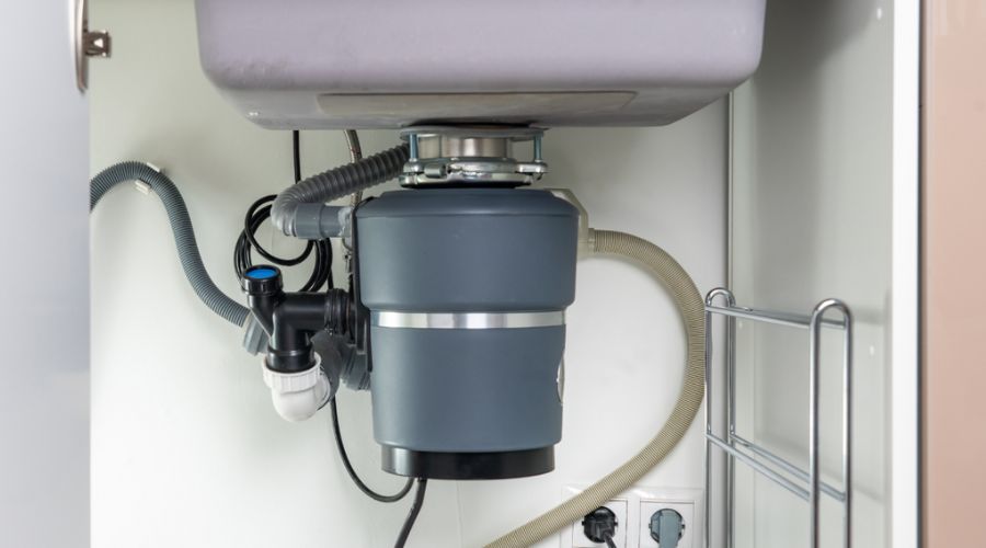 Garbage disposal unit installed under kitchen sink, showcasing plumbing connections and maintenance aspects relevant to preventing clogs.