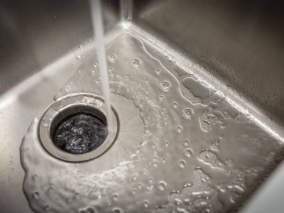 Running cold water into a stainless steel sink with a garbage disposal, illustrating proper maintenance techniques to prevent clogs and ensure functionality.