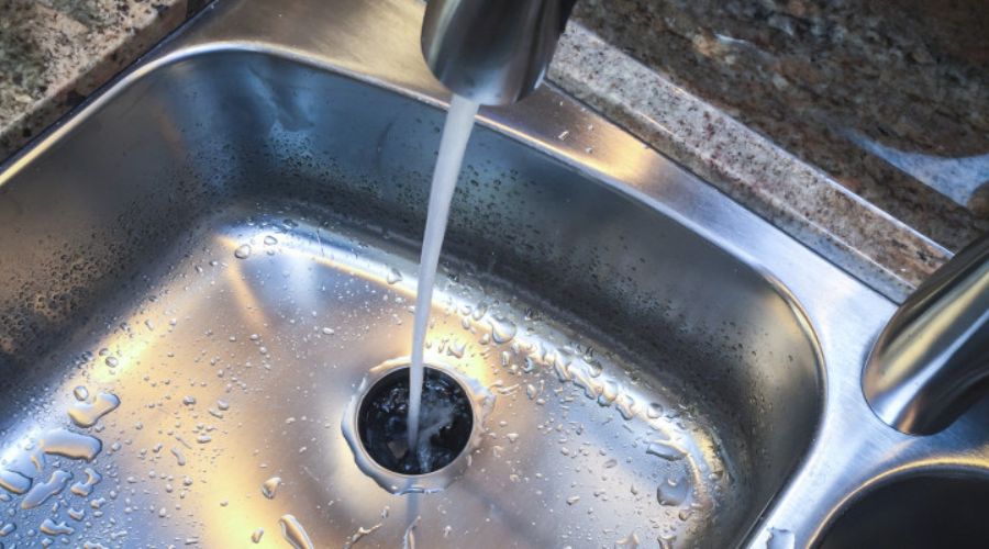 Water flowing from a faucet into a stainless steel sink, highlighting the drain area, relevant to drain cleaning services and plumbing maintenance.