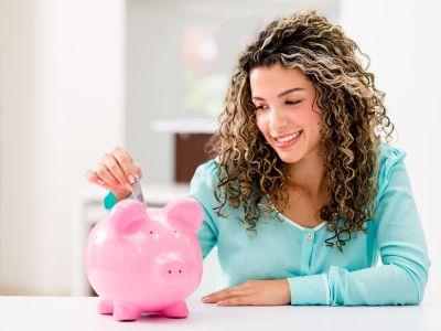 Woman inserting coin into pink piggy bank, symbolizing savings and financial planning, relevant to home improvement and plumbing service investments.